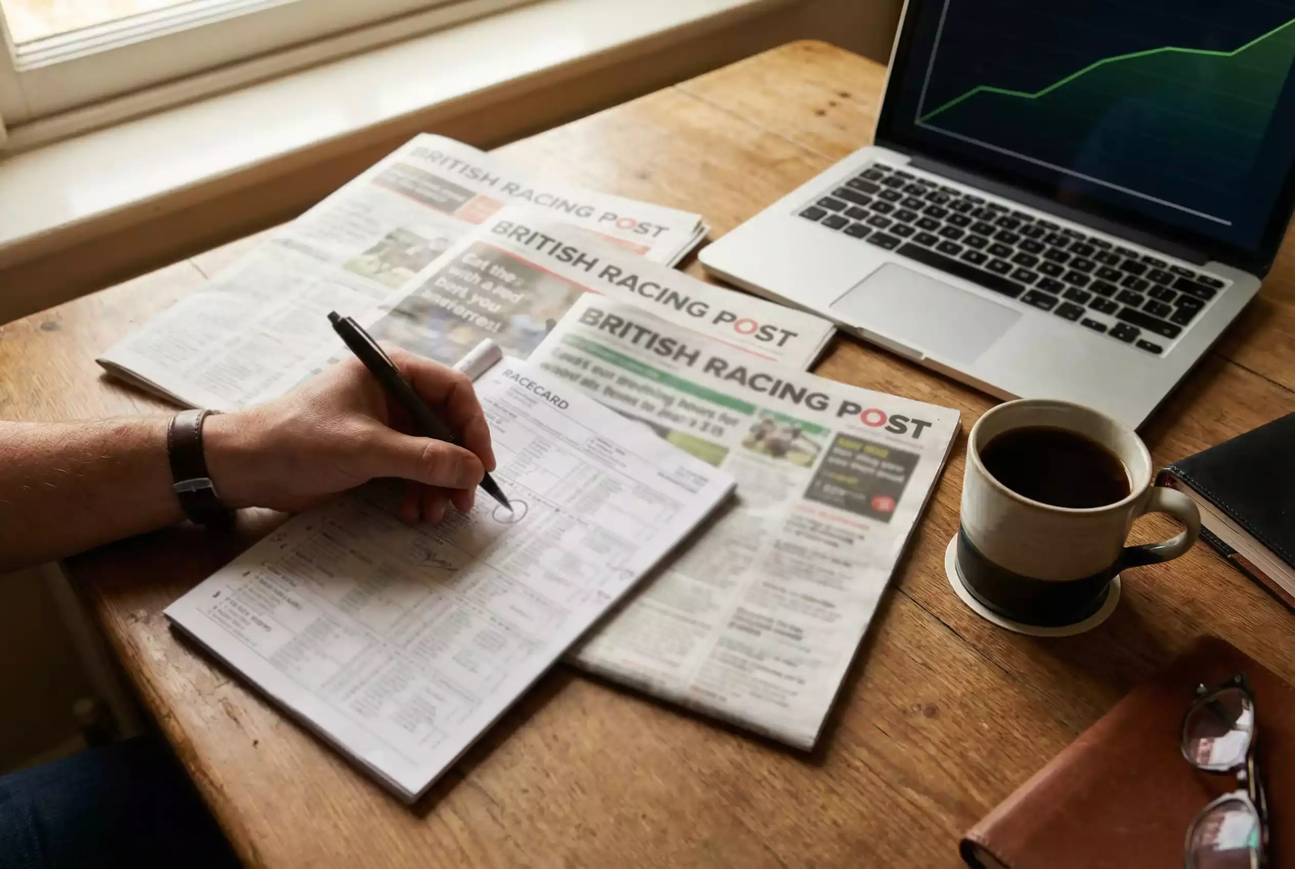 Racing form guide and pen on table with laptop showing betting exchange