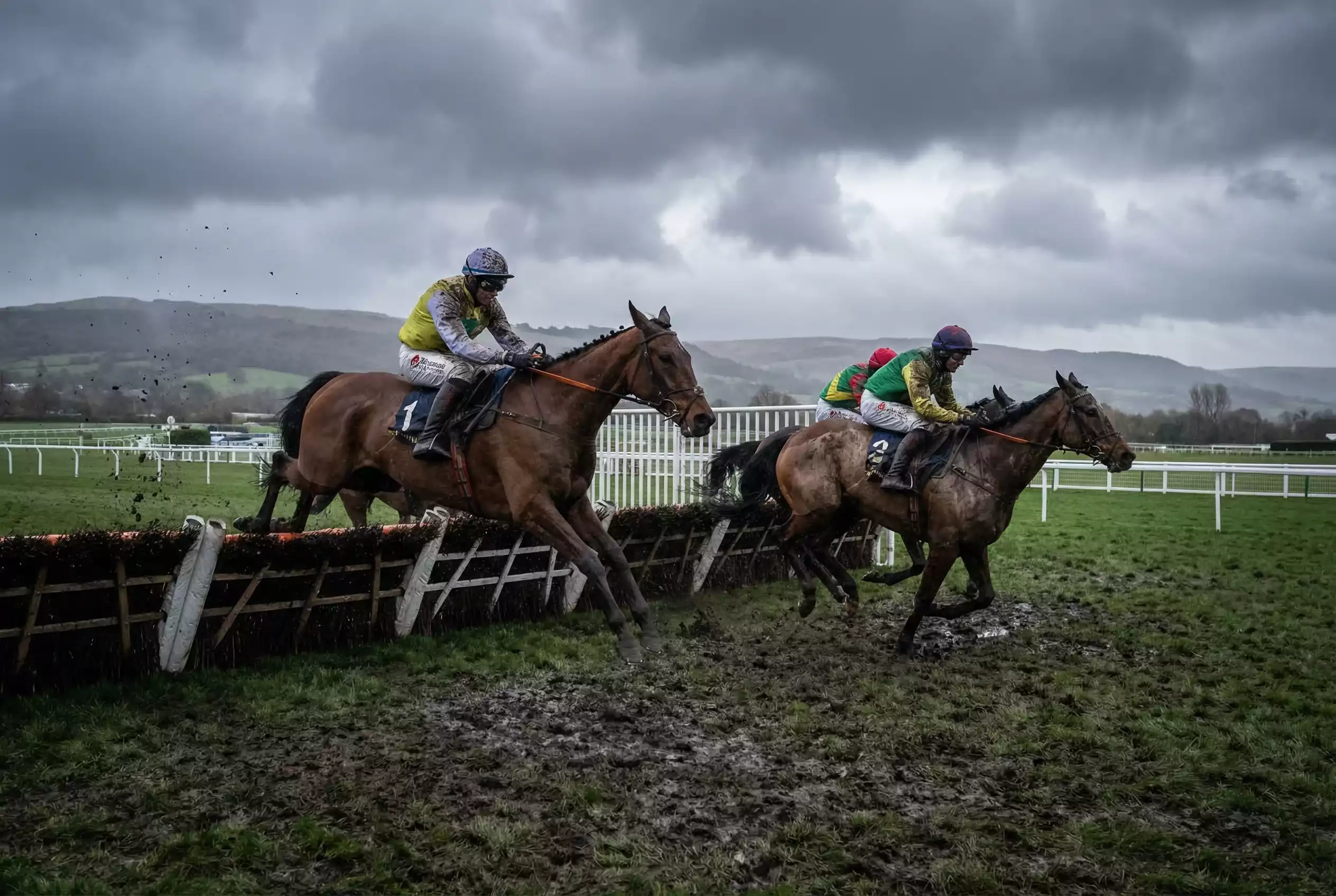 Jump racing horses clearing hurdle on soft winter ground with muddy conditions